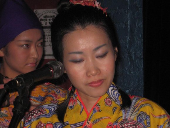 Close-up of KAORI with RENA over her shoulder.