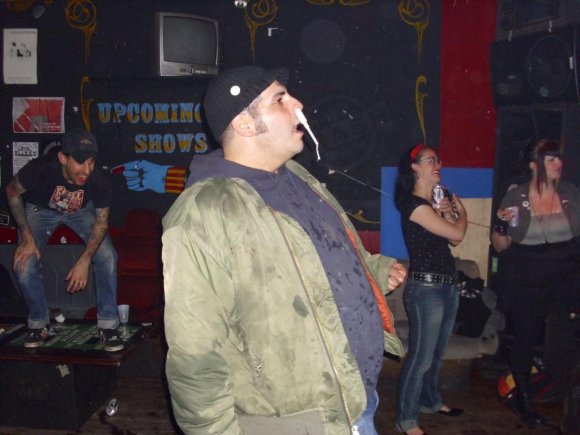 CHAD (AFTERBIRTH) watching ? (with tampon in his nose) as ERIN and ? dance in the background.
