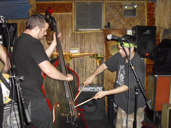 COREY helps DEREK play the bass.